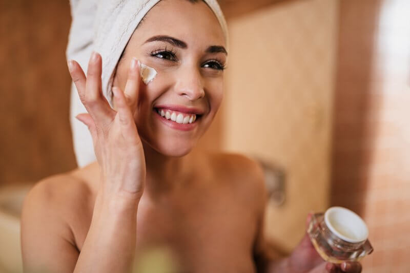 woman wrapped in towel applying face cream in the bathroom