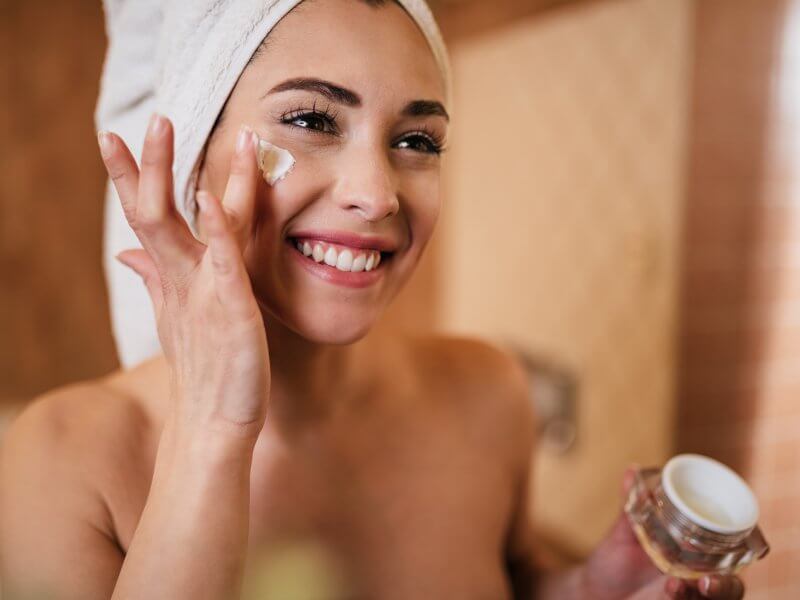 woman wrapped in towel applying face cream in the bathroom