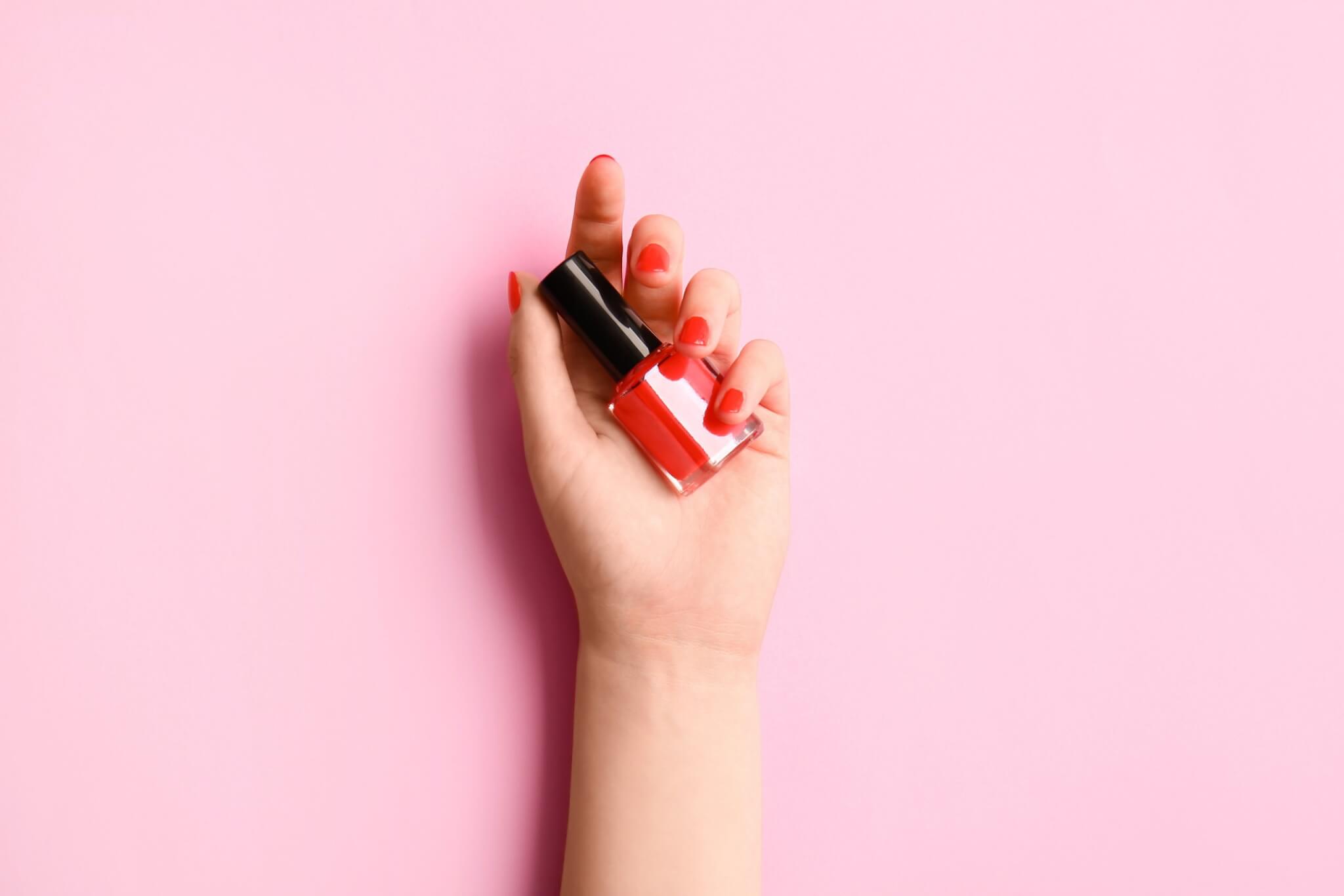 Woman with beautiful manicure holding bottle of gel nail polish on color background